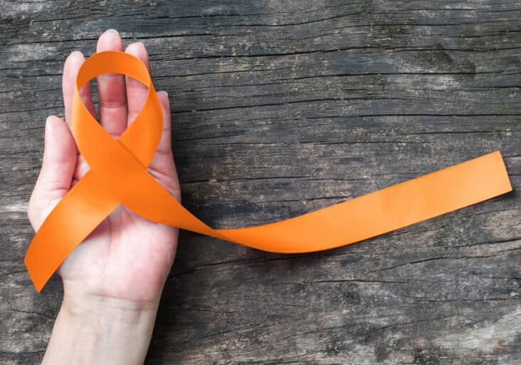 Orange ribbon on old aged background raising awareness on leukemia, kidney cancer, RSD multiple sclerosis Satin fabric color symbolic concept for public support on people living with tumor disease
